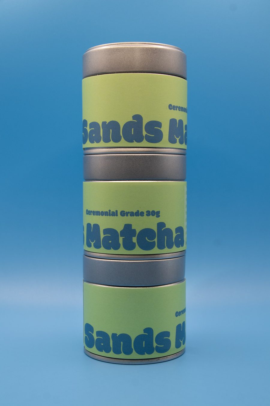 Three stacked Sands Matcha tins with green wrap labels